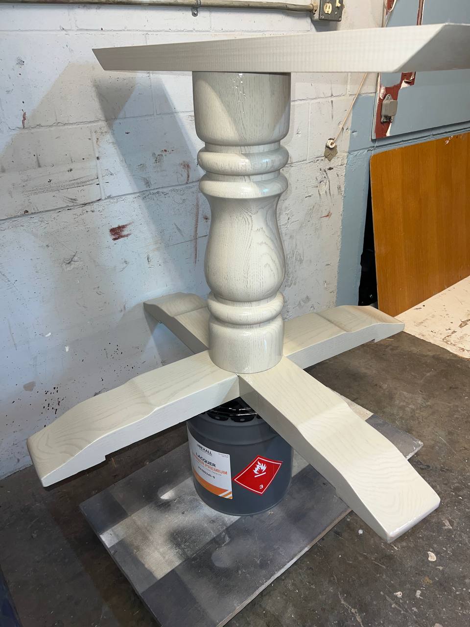 A partially assembled white wooden table base with a turned pedestal and cross supports.