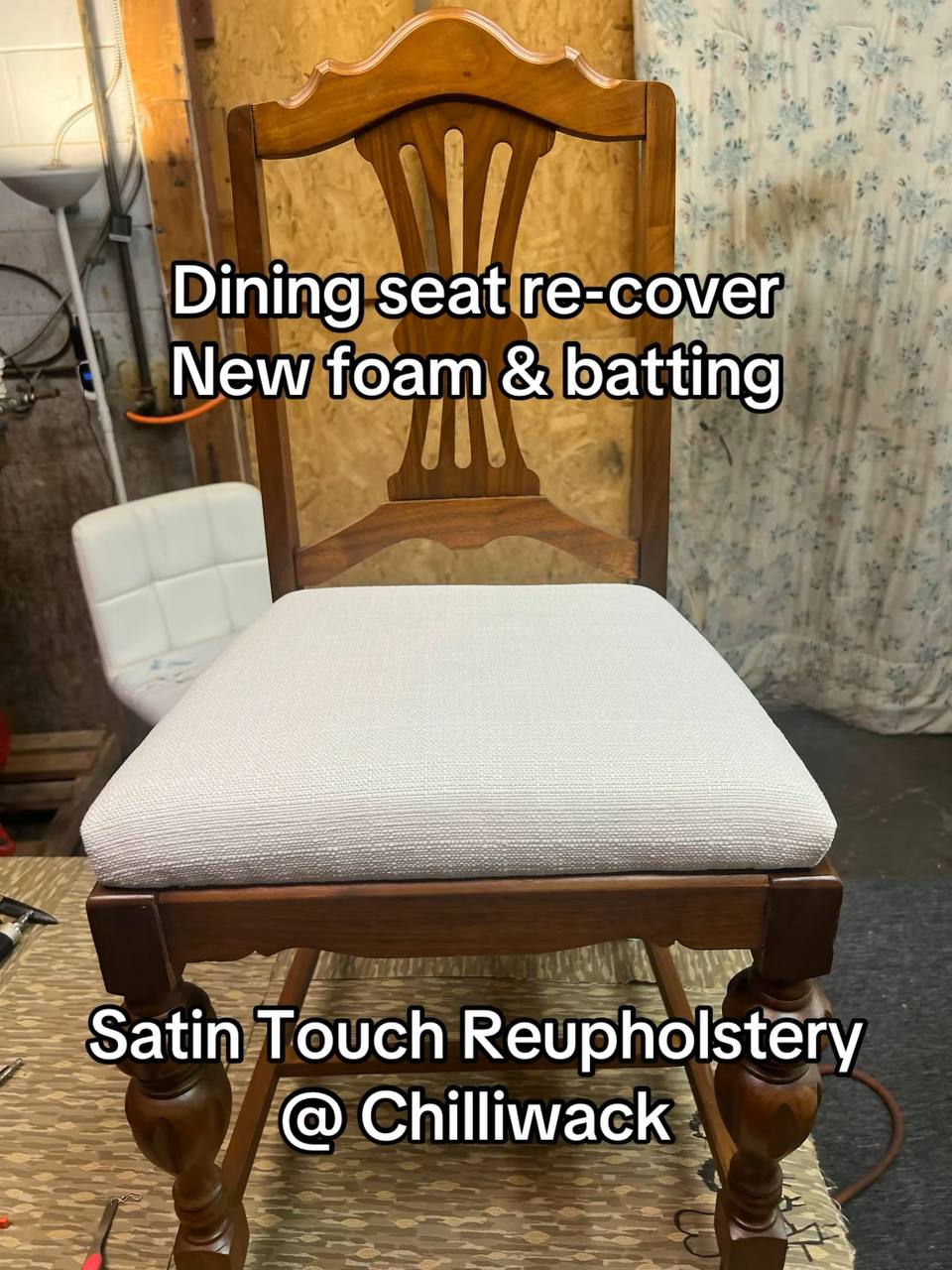 A wooden dining chair with a medium to dark-toned hardwood frame, featuring turned legs and a vertical slat backrest with a curved top rail, upholstered in white-colored fabric