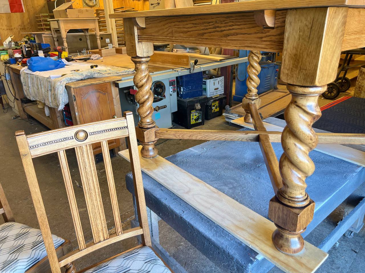 Refinished wooden dining table with carved legs and a dining chair featuring light wood frame and reupholstered patterned fabric seat