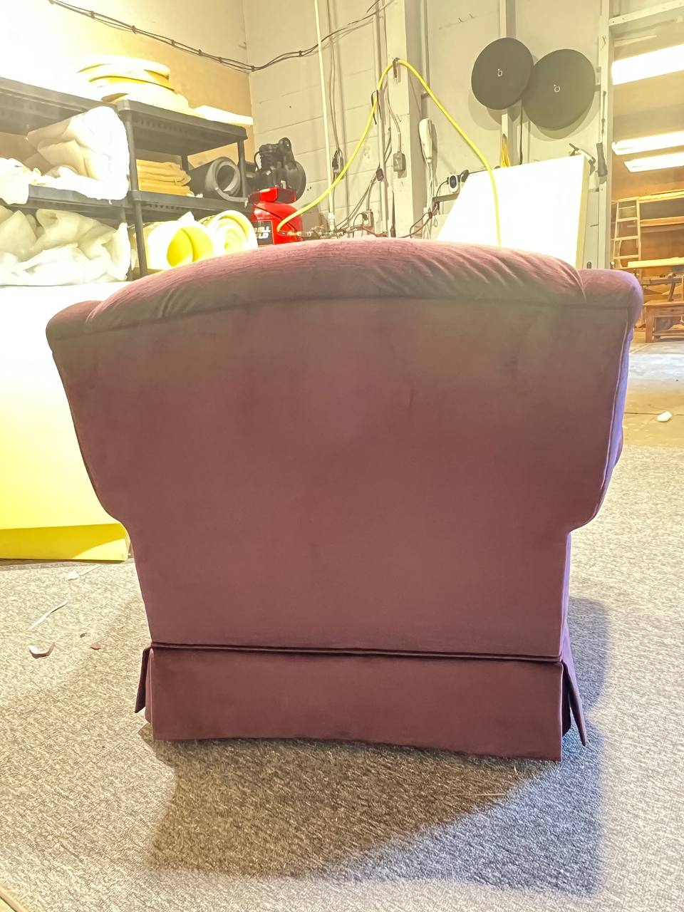 The back of plush rolled-arm armchair upholstered in solid plum fabric with wooden trim accents.