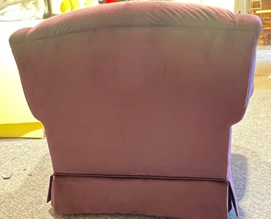 The back of plush rolled-arm armchair upholstered in solid plum fabric with wooden trim accents.