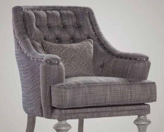 A gray armchair with a tufted backrest, herringbone-patterned fabric, and decorative metallic studs along the arms.