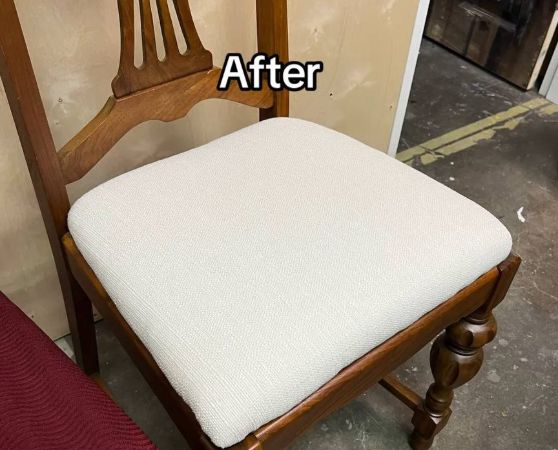 A wooden dining chair with a medium to dark-toned hardwood frame, featuring turned legs and a vertical slat backrest with a curved top rail, upholstered in white-colored fabric