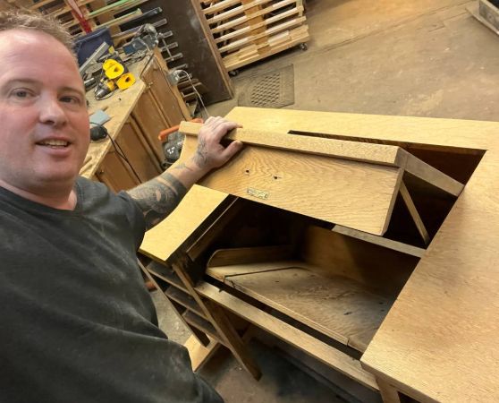 A person working on a light brown wooden desk with an open compartment.