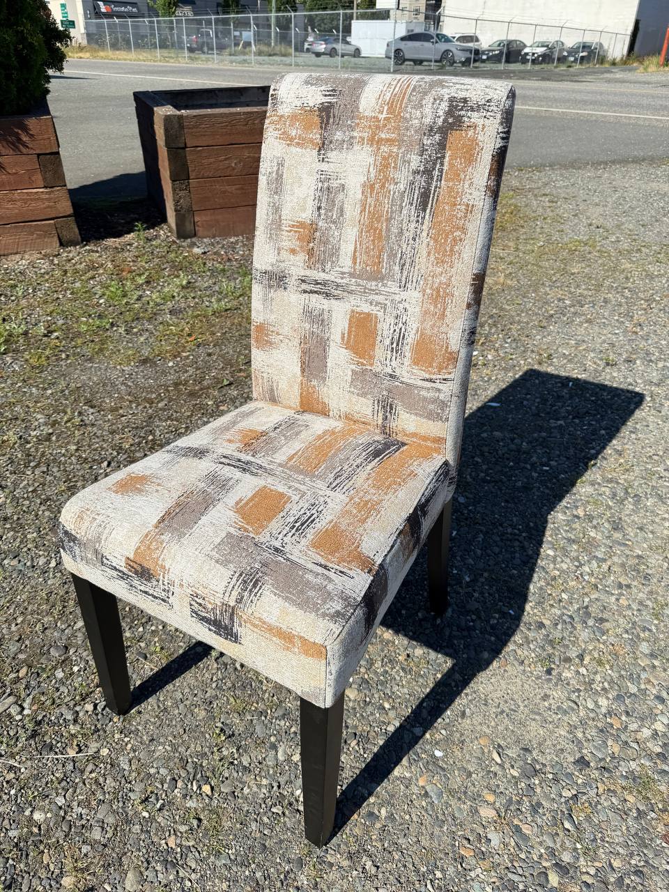 High-back dining chair with abstract beige, brown, and gray upholstery and dark wooden legs.