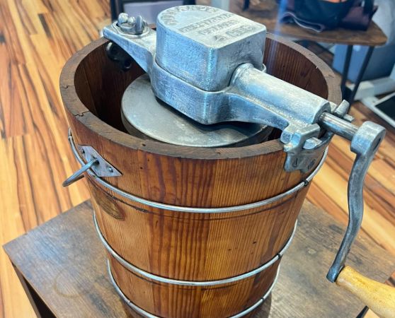 Refinished vintage hand-crank ice cream maker featuring a rustic wood bucket with rich brown grain, silver metal bands, and a cast aluminum crank mechanism.