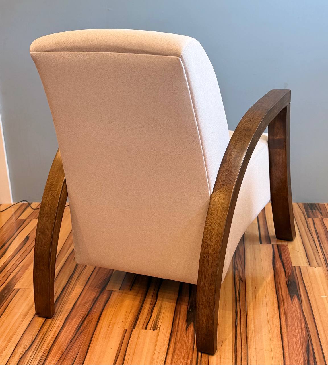 Back of the beige modern armchair with dark wood arms and legs.