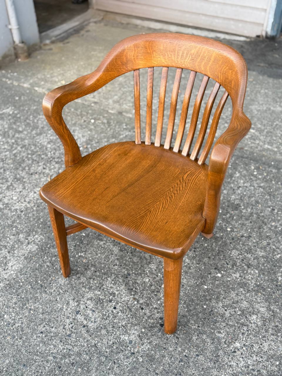 Refinished medium brown vintage wooden banker’s chair with curved armrests and spindle back