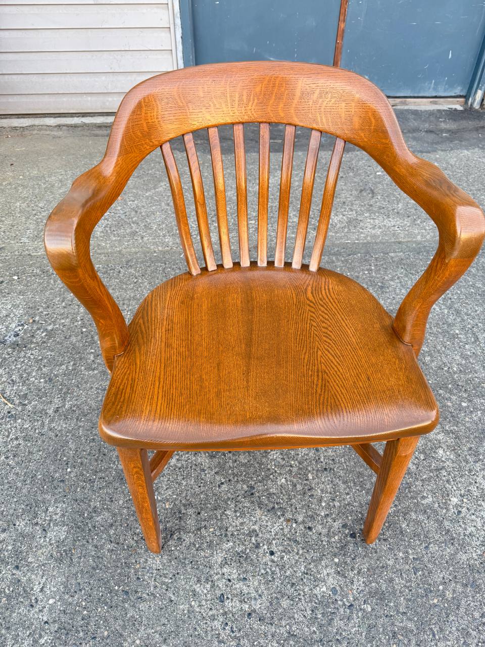 Refinished medium brown vintage wooden banker’s chair with curved armrests and spindle back