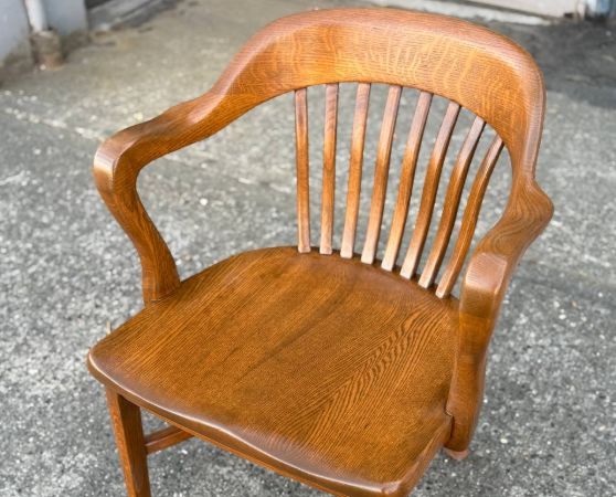 Refinished medium brown vintage wooden banker’s chair with curved armrests and spindle back