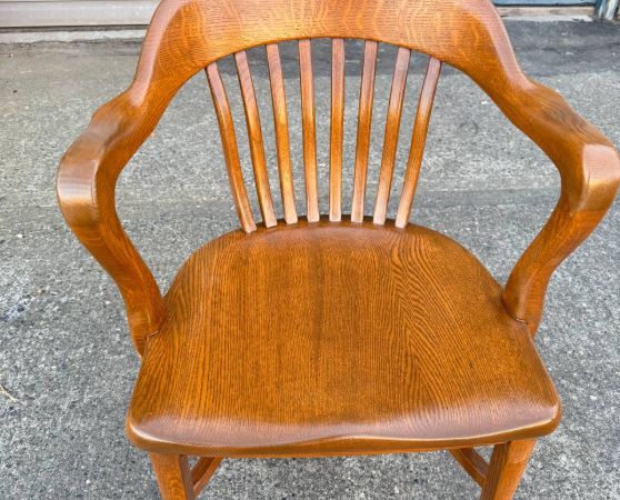 Refinished medium brown vintage wooden banker’s chair with curved armrests and spindle back