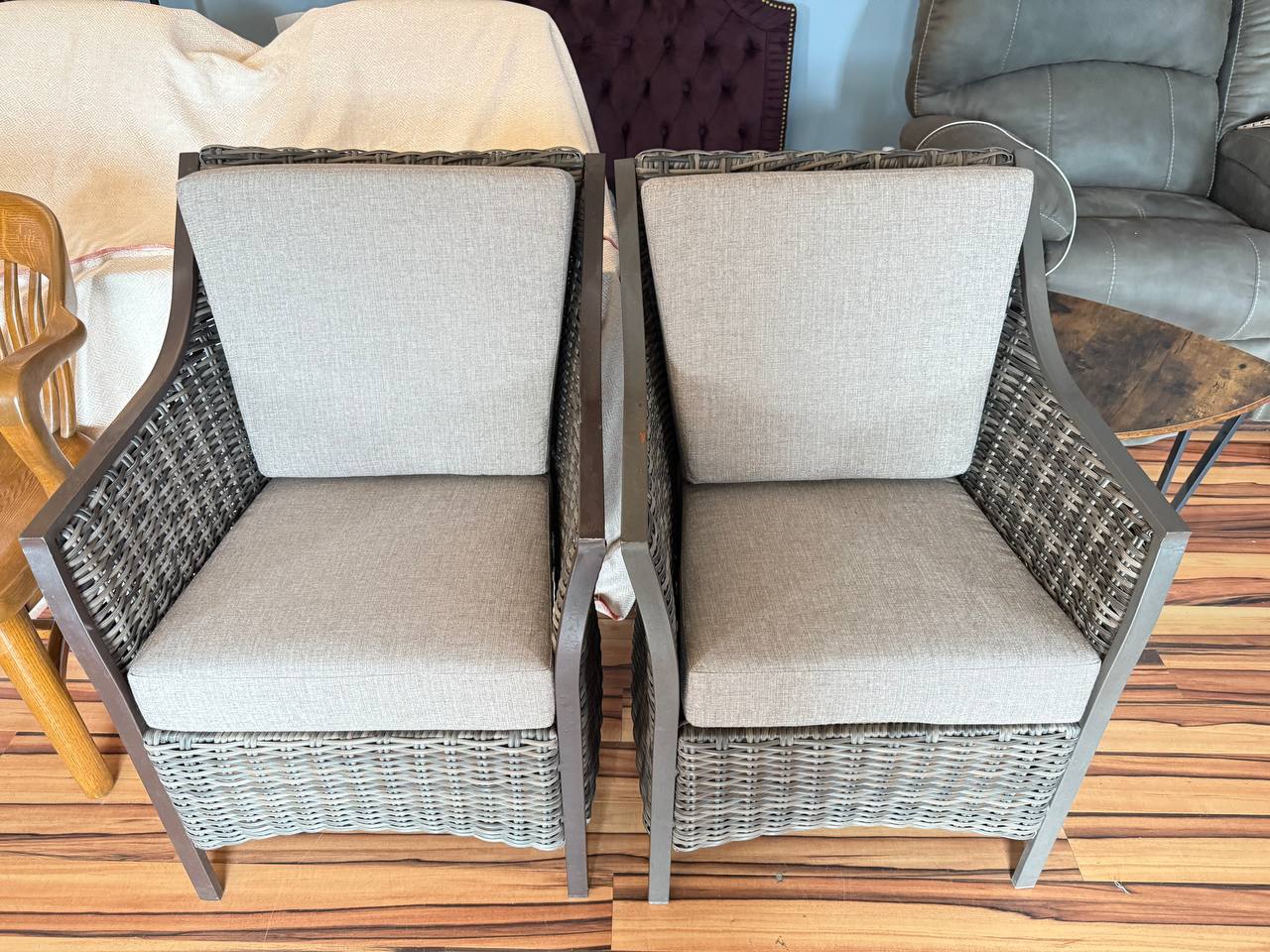Outdoor wicker armchairs with light beige cushions and dark wicker frame.