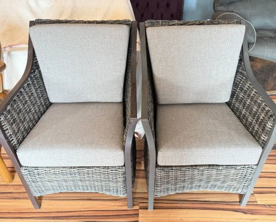 Outdoor wicker armchairs with light beige cushions and dark wicker frame.