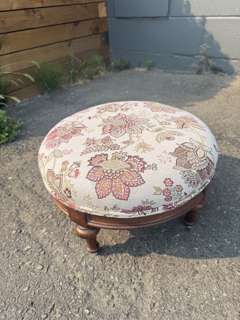 Round ottoman with a vintage style, upholstered in multicolored floral fabric