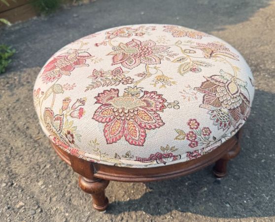Round ottoman with a vintage style, upholstered in multicolored floral fabric