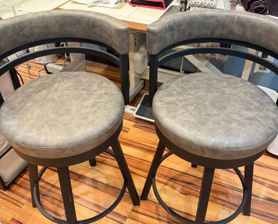 Set of round swivel bar stools with gray leather-look upholstery, black metal base, and curved backrest in a modern contemporary design