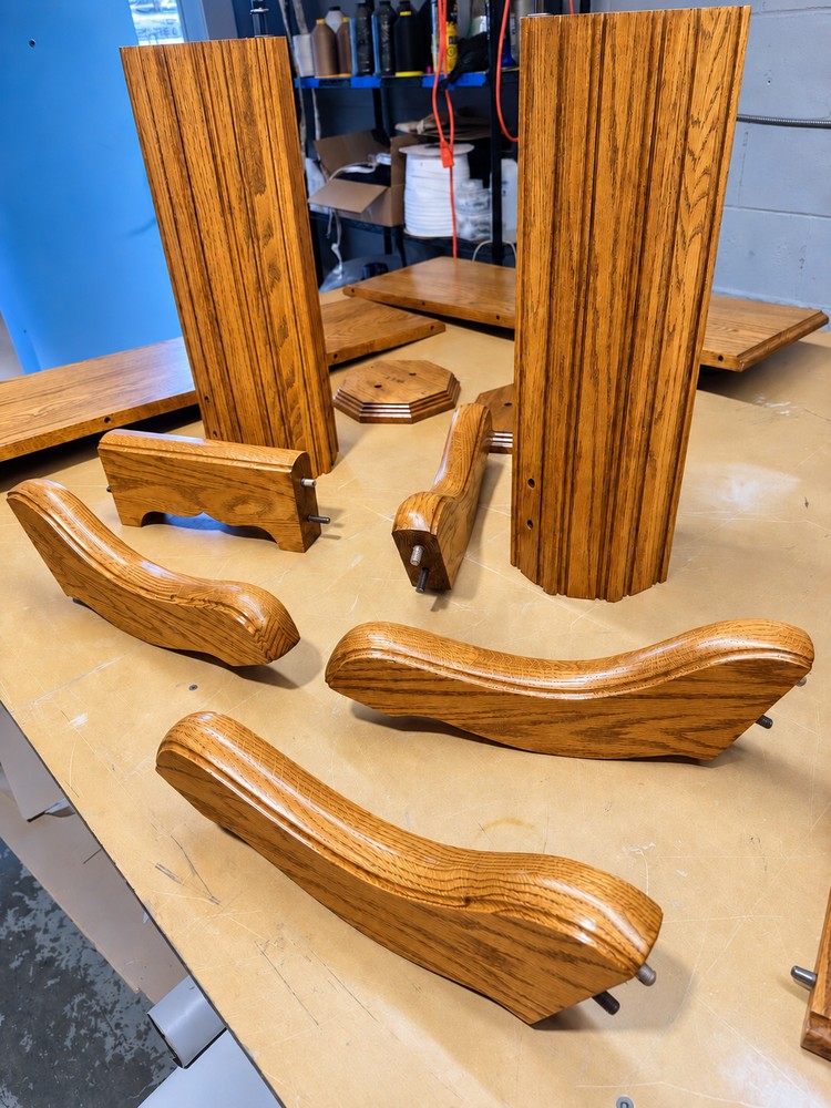 Disassembled oak dining table base with two pedestal columns, curved feet, rails and fittings arranged on a workshop bench.