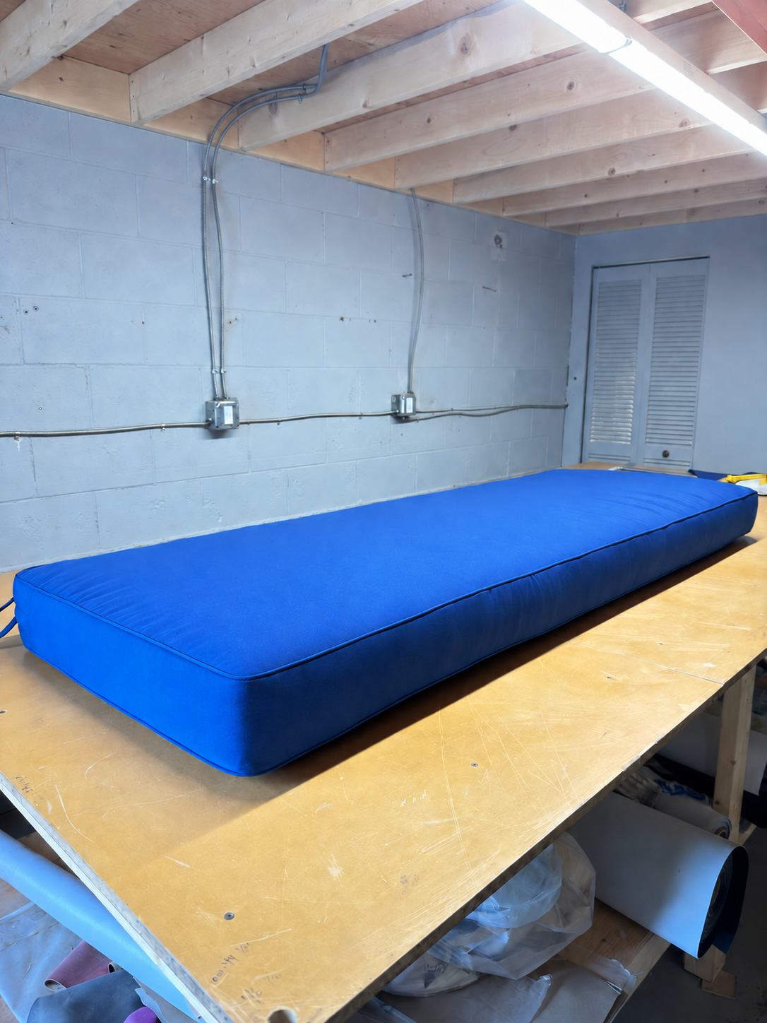 Blue upholstered bench cushion with matching piping, shown on the worktable at Satin Touch.