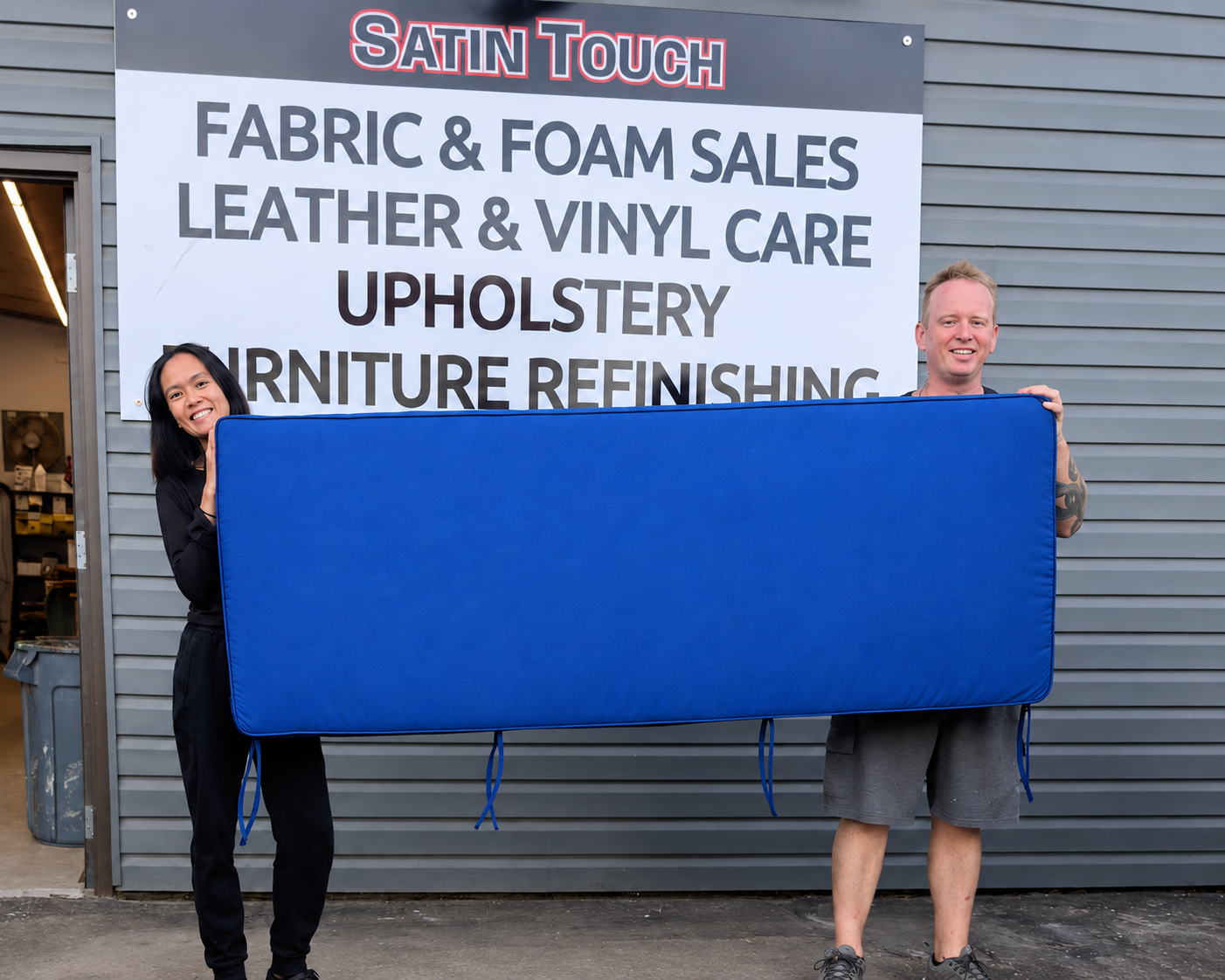Anthony and Janine showing a completed blue bench cushion with matching piping and ties outside Satin Touch in Chilliwack.