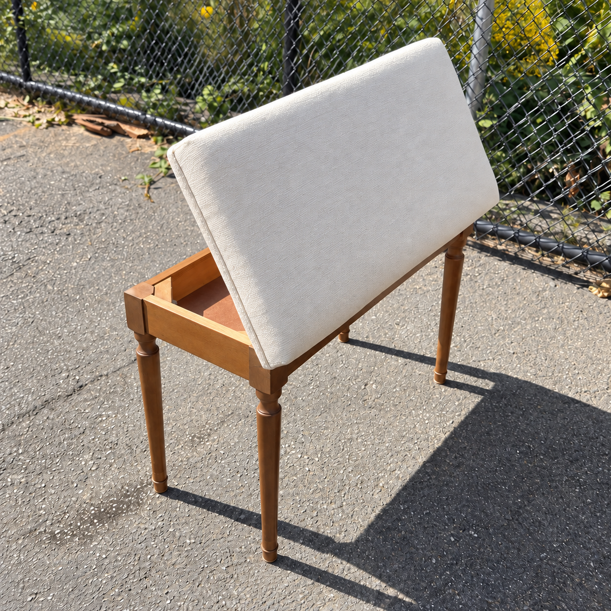 Piano bench with its lid raised, showing the cream textured upholstery and matching edge trim.