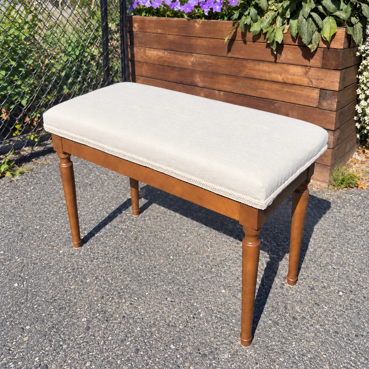 Wooden piano bench with a cream upholstered seat, matching decorative trim and turned legs.